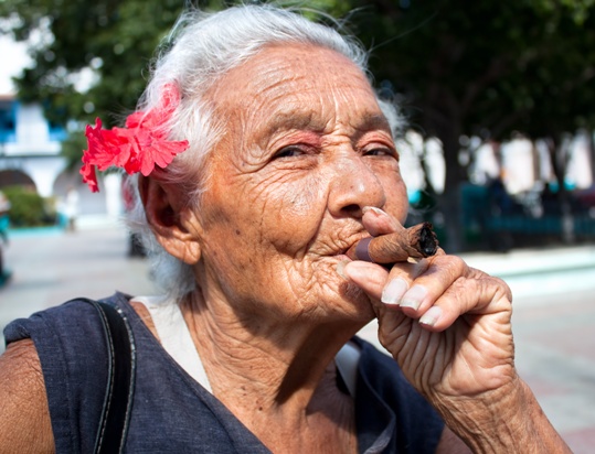 Old wrinkled woman with red flower smoking cigar. Cuba